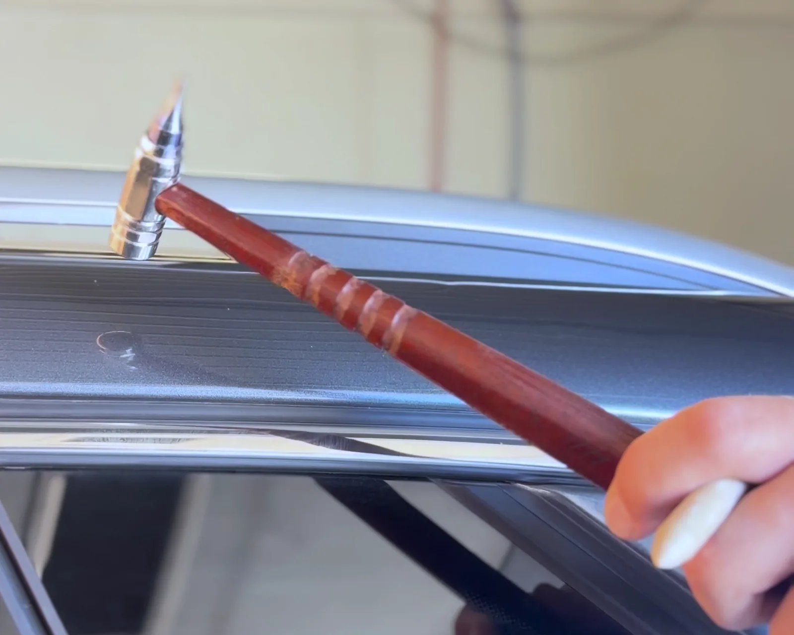 A tap down tool on the edge of a roof rail, beside a small dent